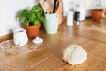 Raw dough for pizza with ingredients placed on wooden table. White ceramic brick wall background