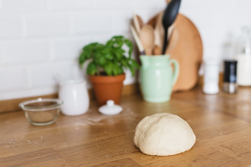 Fototapeta na wymiar Raw dough for pizza with ingredients placed on wooden table. White ceramic brick wall background