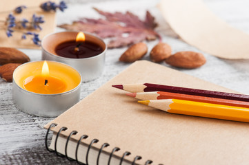 Fototapeta na wymiar Craft notebook and pencils, lit candles