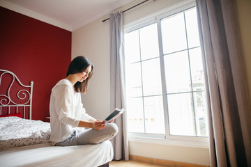 Woman reading book on bed in the morning