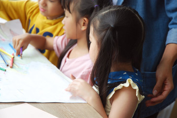 Teachers are teaching drawing on white paper to three children in holiday weekend. Background blur