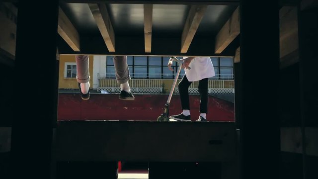 Young guys jumping and doing tricks on a scooter in a skatepark