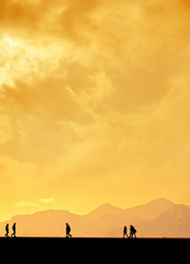 Silhouetted people walking over mountains and orange sunset sky