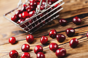Naklejka na ściany i meble Fresh red cherries in metal market basket and scattered berries on old brown wooden table. Business concept