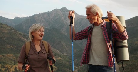 Positive mature caucasian couple trekking in mountains with backpacks, enjoying their adventure 4k