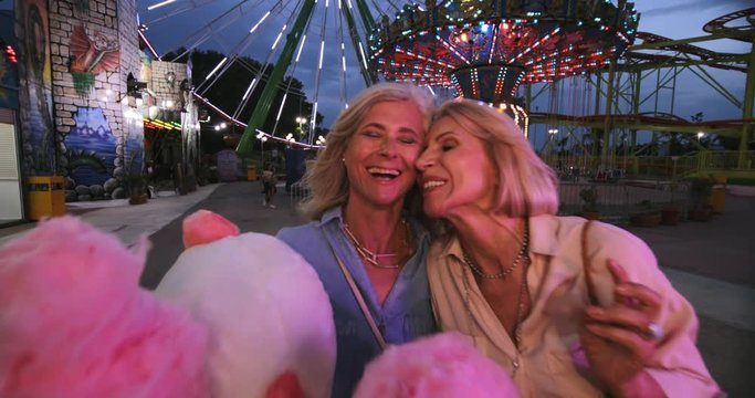 Mature women eating cotton candy and having fun at funfair