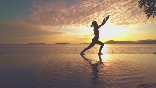 Silhouette of healthy woman doing yoga on the resort pool near the beach at sunrise time. Shot in 4k resolution