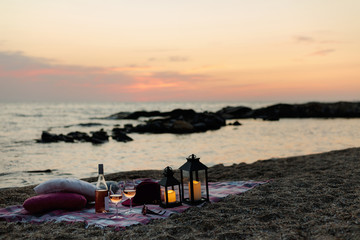 Fototapeta na wymiar Summer sea sunset. Romantic picnic on the beach. Bottle of wine, glasses, candles, plaid and pillows.