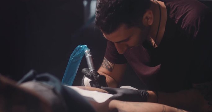 Professional tattooist using tattoo machine and working on client's tattoo