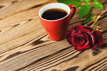 Full cup of black coffee near one red rose on green sprig on old wooden table with copy space. Saint Valentine's Day concept