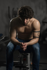 Fototapeta na wymiar Young attractive man resting in gym after exercising, male posing