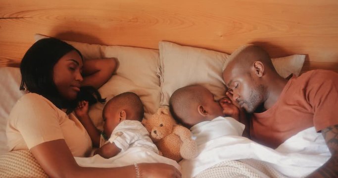 Young parents with little children sleeping and embracing in bed