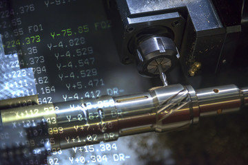 The CNC turning or lathe machine cutting groove slot at the brass shaft  by the milling spindle with the G-code data in background. Hi - technology manufacturing process.