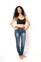 Cheerful slim curly brunette woman standing in blue jeans and a black shirt on a white background