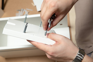 Assembling of furniture, closeup of tool in hand. Mounting screw is screwed into hole board.