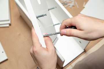 Assembling of furniture, closeup of tool in hand. Mounting screw is screwed into hole board.