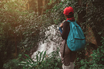 Freedom hipster traveler woman standing with backpack and enjoying a beautiful waterfall in nature forest.