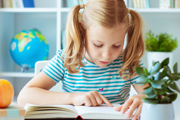 Portrait of a cute little girl read book at the table in classroom