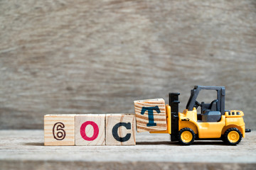 Toy forklift hold block T to complete word 6 oct on wood background (Concept for calendar date in...