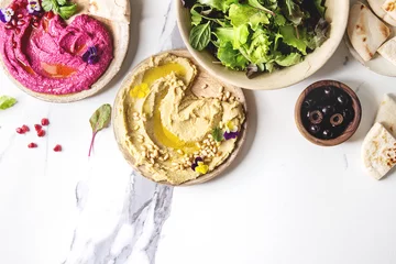 Tafelkleed Variety of homemade traditional and beetroot spread hummus with pine nuts, olive oil, pomegranate served on ceramic plates with pita bread and green salad on white marble background. Flat lay, space. © Natasha Breen