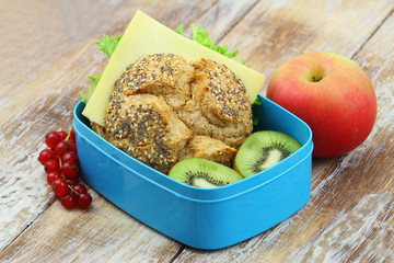 Healthy school lunch box containing whole grain cheese roll with lettuce, kiwi fruit and apple
