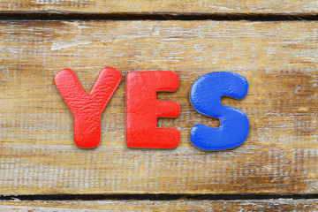 Word Yes written with colorul letters on rustic wooden surface
