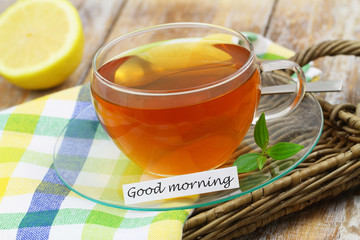 Good morning card with green  tea in transparent cup on wicker tray, closeup
