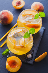 ripe peaches cocktail with ice and fresh mint on a black table. refreshing summer drink
