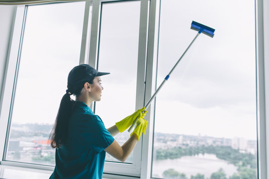 A picture of cleaner works at window. She cleans it with mop. Girl is concentrated. She does it careful.