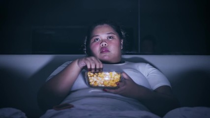 Overweight woman enjoying a bowl of popcorn at night on the bed before sleep. Shot in 4k resolution - Powered by Adobe