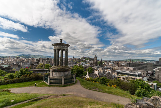 Edinburgh, Scotland, UK - June 13, 2012: Wide shot. Brown stone Donald Stewart Monument on Calton Hill. Background is almost 180 degrees panorama of Edinburgh under blue sky with white clouds.