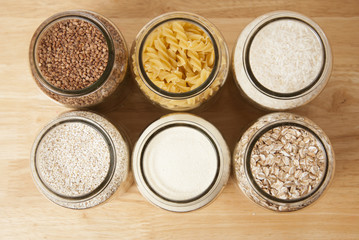 Various uncooked cereals, grains, and pasta for healthy cooking in glass jars on wooden table. Top view. Clean eating, balanced dieting food
