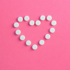 Heart shaped of white pills on pink background