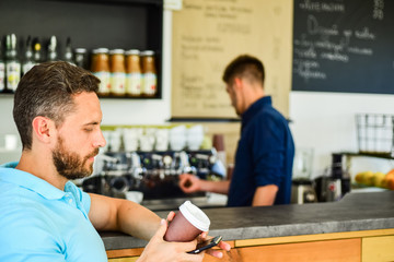 Man holds paper cup with coffee barista guy stand on background. Client got his drink. Drinks to go useful option in modern cafe. Have sip of energy. Man client with beard enjoy coffee in paper cup