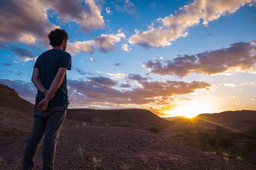 A young man watching the sunset in a beautiful valley. Some clouds in the sky, Beginning, reflection, relaxing, meditating, peaceful, insights concepts.