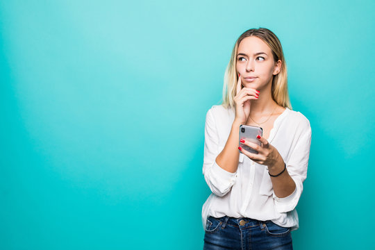 Portrait Of A Thinking Young Woman Using Mobile Phone Isolated Over Blue Background