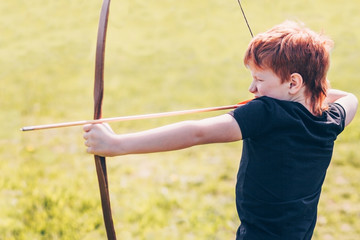 Redheaded boy aiming for a target with a bow arrow