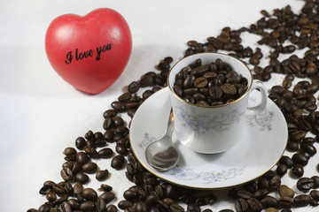 Composition of a white cup of coffee on a pile of coffee beans and a red heart in the background....