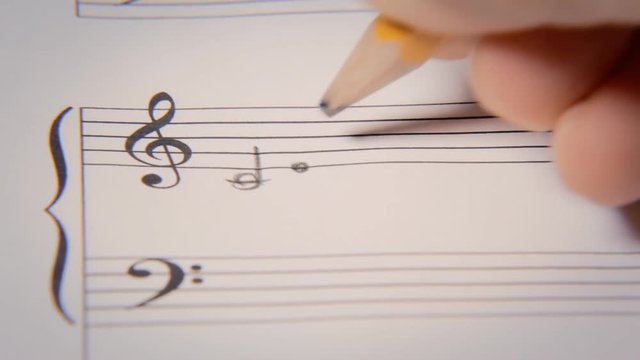Composing music on a paper sheet with rows and symbols. Detail front shot.
