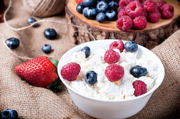 Berries of raspberries, strawberries, blueberries on a a baggy background, cottage cheese with berries in a white plate. Proper nutrition