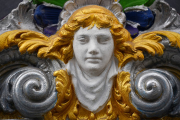 A golden painted angel face between an ornamnet on an old house in Berlin Kreuzberg.	