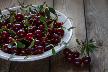 Ripe cherry in a white plate on a wooden table. Macro. Rustic style