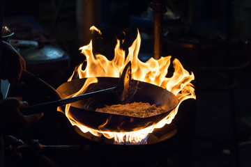 Movement the chef cooking Stir fried rice noodles on stove with flame at China town or Yaowarat Road in Bangkok, Thailand 
