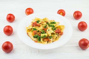 Italian pasta with tomatoes and pesto sauce, on a wooden background