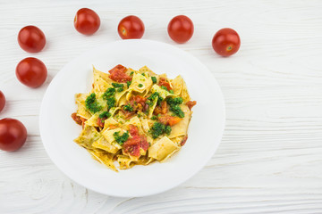 Italian pasta with tomatoes and pesto sauce, on a wooden background