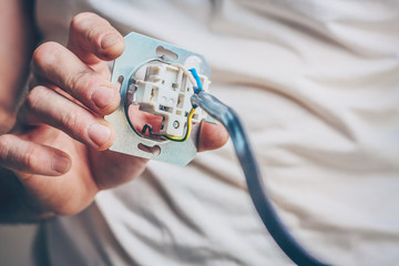 The electrician performs electrical work - a ready assembled socket before installing into the wall