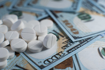 White pills on one hundred dollar bills close up. Medicine price concept.