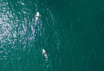 Aerial view of 2 paddle boarders on a blue / green sea 