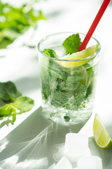 Cold refreshing summer Mojito lemonade in a glass on a white background. Lime, mint, ice.