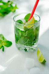 Cold refreshing summer Mojito lemonade in a glass on a white background. Lime, mint, ice.